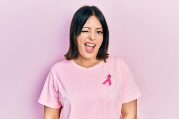 Fototapeta premium Young hispanic woman wearing pink cancer ribbon on t shirt winking looking at the camera with sexy expression, cheerful and happy face.