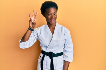 Young african american girl wearing karate kimono and black belt showing and pointing up with fingers number three while smiling confident and happy.