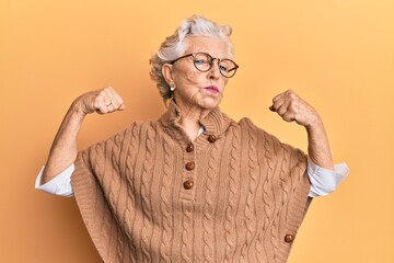Senior grey-haired woman wearing casual clothes and glasses showing arms muscles smiling proud....