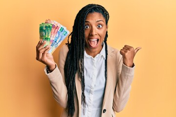 African american woman holding south african rand banknotes pointing thumb up to the side smiling happy with open mouth