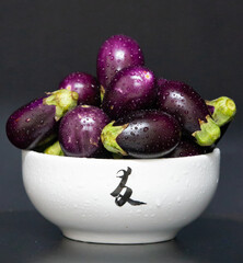 Mini wet eggplants in white pot with dark background