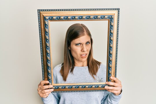 Beautiful caucasian woman holding empty frame clueless and confused expression. doubt concept.