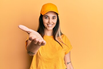 Young hispanic woman wearing delivery uniform and cap smiling friendly offering handshake as greeting and welcoming. successful business.