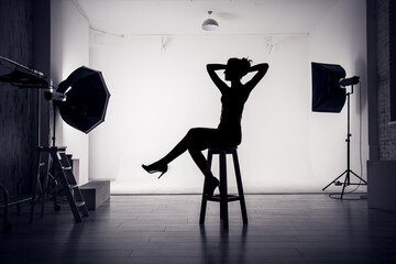 Silhouette of a young girl in the studio sitting on a chair with her hands behind her head