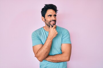 Handsome hispanic man with beard wearing casual clothes with hand on chin thinking about question, pensive expression. smiling with thoughtful face. doubt concept.