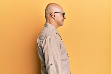 Middle age bald man wearing casual clothes and glasses looking to side, relax profile pose with...