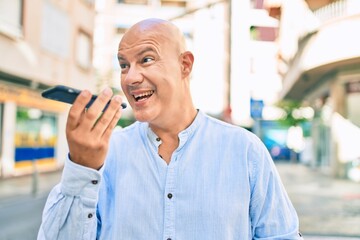 Middle age bald man smiling happy sending audio message using smartphone at the city.