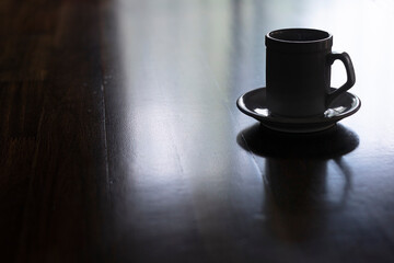 Cup of coffee with saucer on wood table. Figure in shadows. Reflection on table