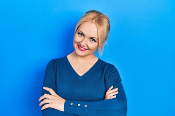 Young blonde woman wearing casual blue sweater happy face smiling with crossed arms looking at the camera. positive person.