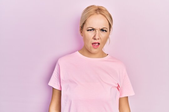 Young blonde woman wearing casual pink t shirt in shock face, looking skeptical and sarcastic, surprised with open mouth