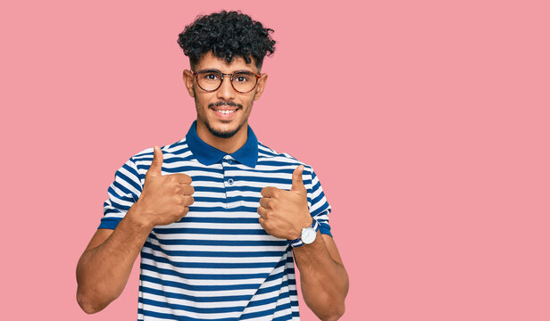Young arab man wearing casual clothes and glasses success sign doing positive gesture with hand, thumbs up smiling and happy. cheerful expression and winner gesture.