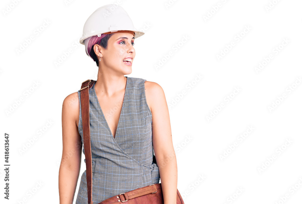 Sticker young beautiful woman wearing architect hardhat and leather bag looking away to side with smile on f