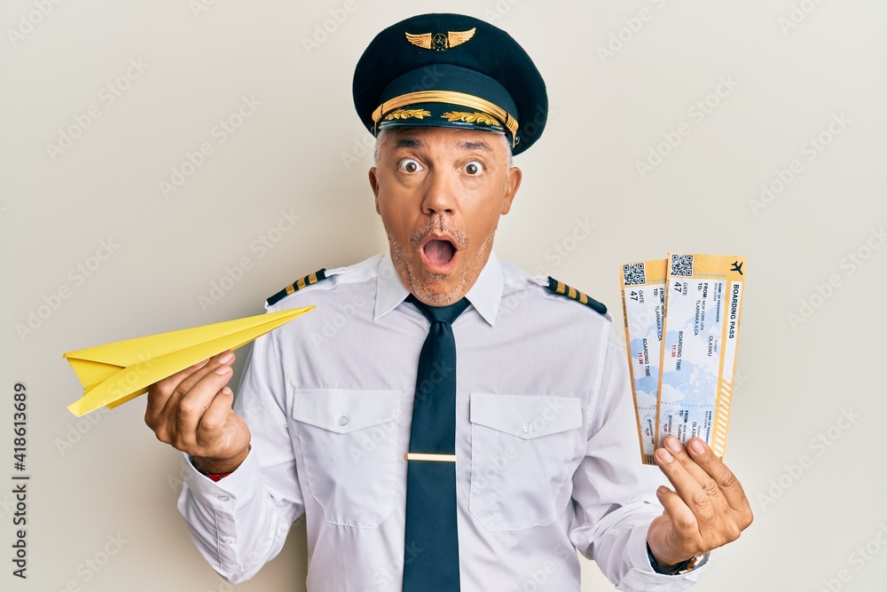 Sticker handsome middle age mature pilot man holding paper plane and boarding pass afraid and shocked with s