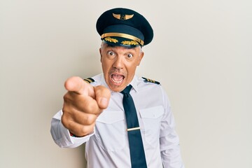 Handsome middle age mature man wearing airplane pilot uniform pointing displeased and frustrated to the camera, angry and furious with you