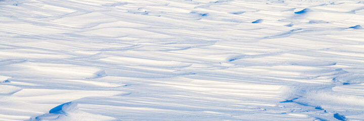 Beautiful winter background with snowy ground. Natural snow texture. Wind sculpted patterns on snow surface. Arctic, Polar region.