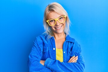 Young blonde girl wearing casual clothes and glasses happy face smiling with crossed arms looking...