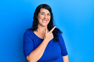 Fototapeta premium Plus size brunette woman wearing casual blue shirt cheerful with a smile of face pointing with hand and finger up to the side with happy and natural expression on face