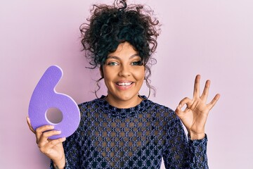 Young hispanic woman holding number six doing ok sign with fingers, smiling friendly gesturing...
