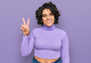 Young hispanic woman with curly hair wearing casual clothes smiling looking to the camera showing...
