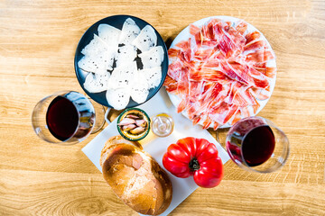 Typical Catalan or Spanish food. Bread with tomato, Iberian ham, glass of black wine, goat cheese, oil and garlic. Top view of food products for dinner or tapas on a wooden background.