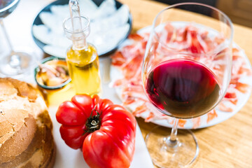 Typical Catalan or Spanish food. Bread with tomato, Iberian ham, glass of red wine, goat cheese, oil and garlic. Food products for dinner or tapas on a wooden background.