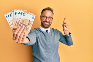 Handsome middle age man holding bunch of euros smiling happy pointing with hand and finger to the side