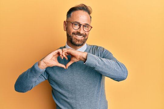 Handsome middle age man wearing glasses smiling in love doing heart symbol shape with hands. romantic concept.