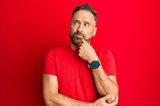 Handsome middle age man wearing casual red tshirt thinking concentrated about doubt with finger on chin and looking up wondering