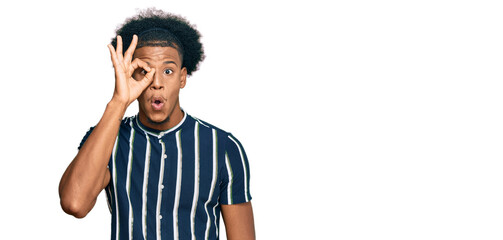 African american man with afro hair wearing casual clothes doing ok gesture shocked with surprised face, eye looking through fingers. unbelieving expression.