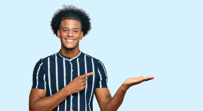 African american man with afro hair wearing casual clothes amazed and smiling to the camera while presenting with hand and pointing with finger.