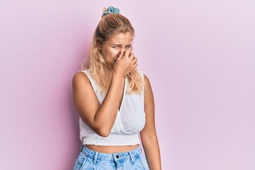 Young blonde girl wearing casual clothes smelling something stinky and disgusting, intolerable...