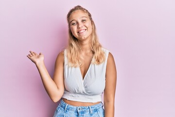 Young blonde girl wearing casual clothes smiling cheerful presenting and pointing with palm of hand looking at the camera.