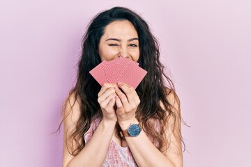 Young hispanic woman covering mouth with cards winking looking at the camera with sexy expression, cheerful and happy face.
