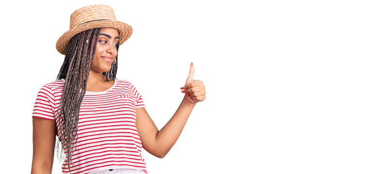 Young african american woman with braids wearing summer hat looking proud, smiling doing thumbs up gesture to the side