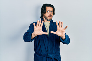 Naklejka premium Middle age caucasian man wearing bathrobe and glasses afraid and terrified with fear expression stop gesture with hands, shouting in shock. panic concept.