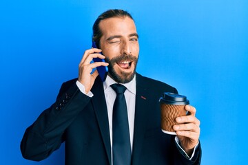 Attractive business man with long hair and beard using smartphone and drinking a cup of coffee...
