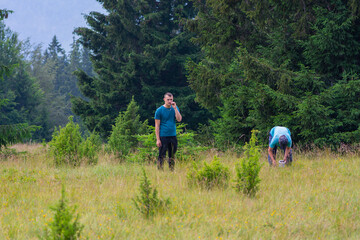 Fototapeta na wymiar Two man in the forest at summer day. Boy holding toothpick in his mouth and man picking fresh wild blueberries