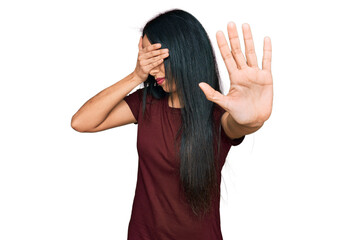 Young hispanic girl wearing casual t shirt covering eyes with hands and doing stop gesture with sad and fear expression. embarrassed and negative concept.