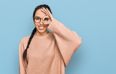 Young hispanic girl wearing casual clothes and glasses doing ok gesture with hand smiling, eye looking through fingers with happy face.