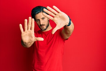 Young hispanic man wearing casual red t shirt doing frame using hands palms and fingers, camera perspective