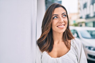 Young hispanic woman smiling happy leaning on the wall at the city.