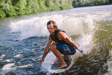 Young athletic man with long hair wakesurfing on waves of river in sunny summer weather. Ttheme outdoor activities in summer. Water sports wakesurf on the board. sliding wakeboarder in water splash