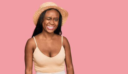 Young black woman wearing summer hat winking looking at the camera with sexy expression, cheerful and happy face.