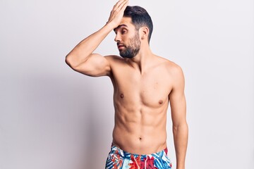 Fototapeta premium Young handsome man with beard shirtless wearing swimwear surprised with hand on head for mistake, remember error. forgot, bad memory concept.