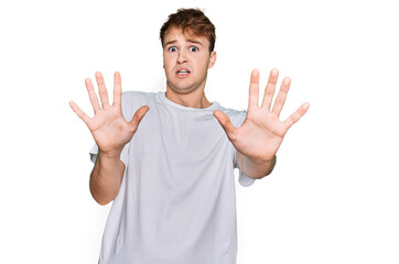 Fototapeta premium Young caucasian man wearing casual white t shirt afraid and terrified with fear expression stop gesture with hands, shouting in shock. panic concept.