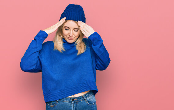 Young caucasian woman wearing wool winter sweater and cap with hand on head for pain in head because stress. suffering migraine.