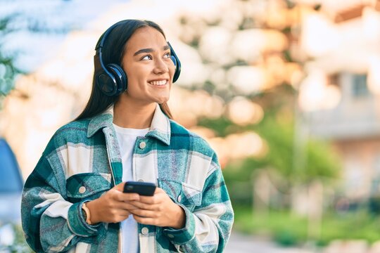 Young latin girl smiling happy using smartphone and headphones at the city.