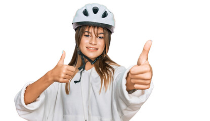 Teenager caucasian girl wearing bike helmet approving doing positive gesture with hand, thumbs up smiling and happy for success. winner gesture.