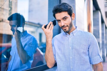 Young hispanic man smiling happy listening audio message using smartphone at city.