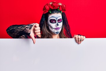 Young woman wearing day of the dead costume holding blank empty banner with angry face, negative sign showing dislike with thumbs down, rejection concept